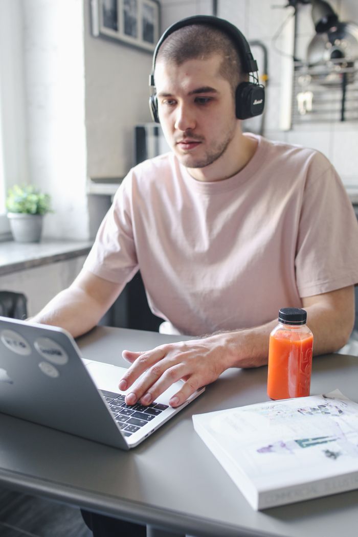 Menus Young man working on laptop with headphones, focused on remote tasks indoors.